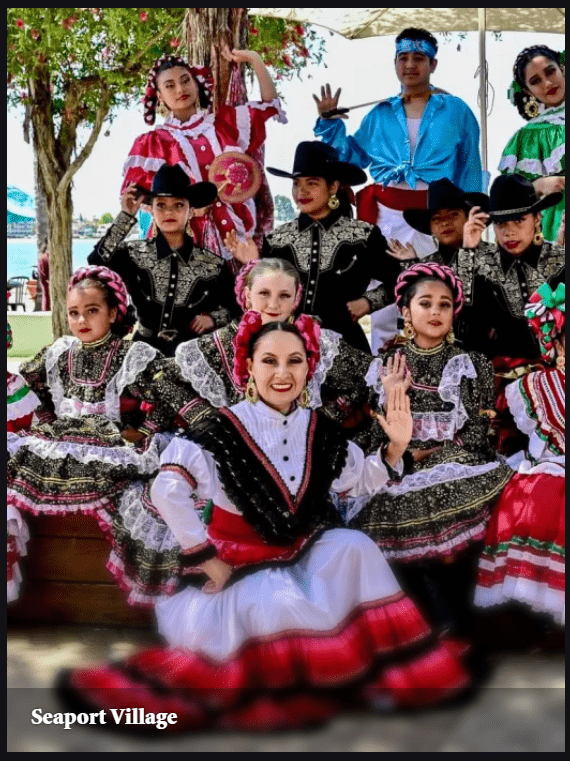 Dancers in vibrant traditional costumes pose joyfully at Seaport Village, showcasing cultural heritage and community celebration.