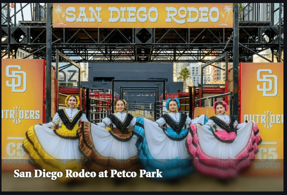 Colorfully dressed dancers in traditional attire perform at the San Diego Rodeo, set against the backdrop of Petco Park's entrance.