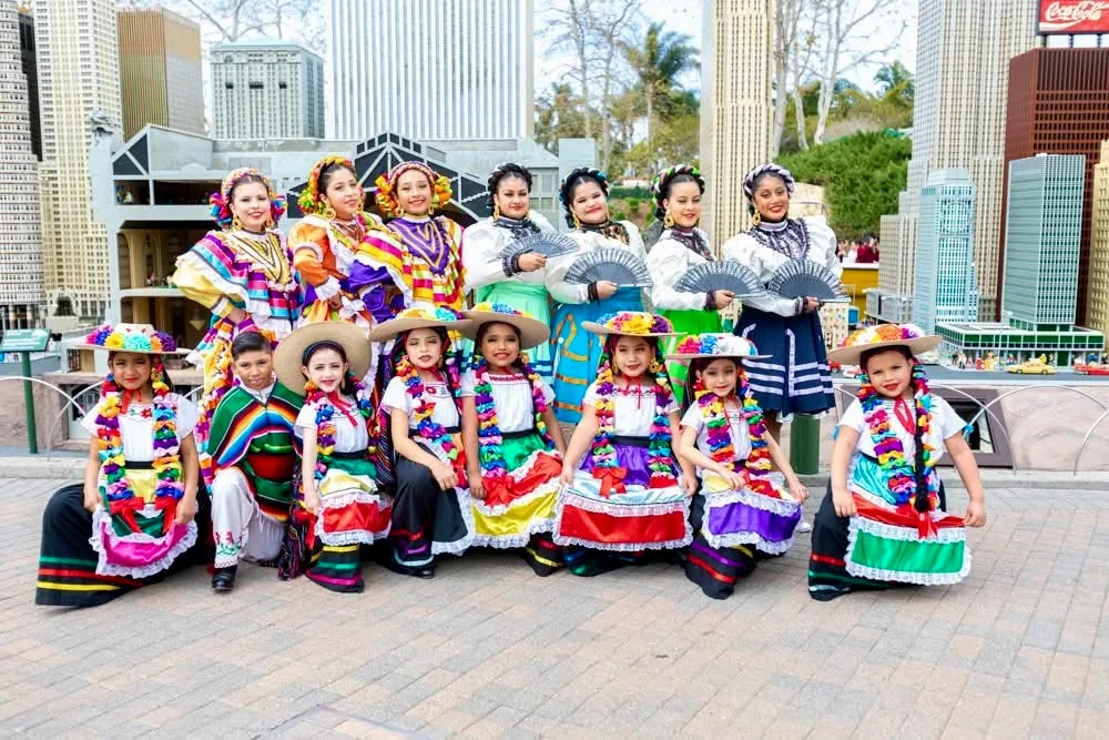 Dancers in colorful traditional Mexican attire pose for a group photo against a backdrop of a cityscape, showcasing cultural heritage and celebration.