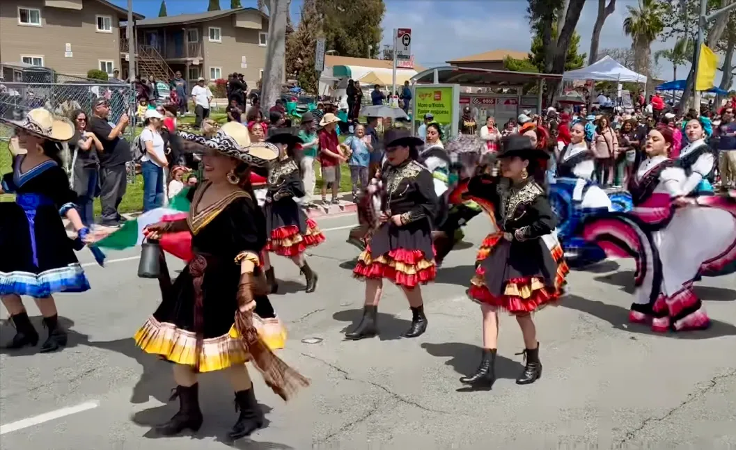 Dancers in vibrant traditional costumes perform at a lively parade, showcasing cultural heritage and engaging an enthusiastic crowd.