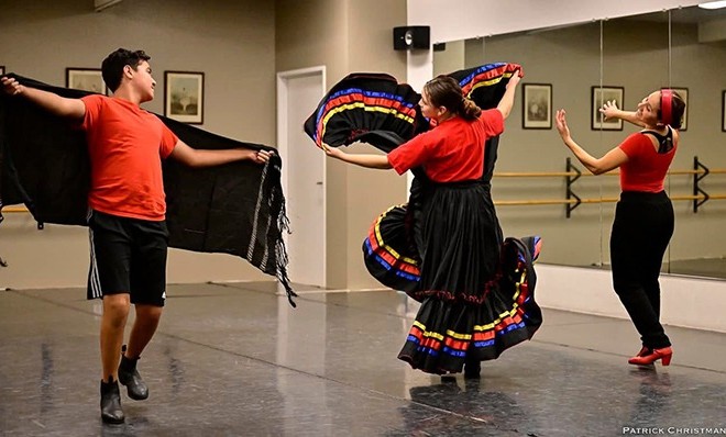 Two dancers practice traditional Mexican ballet, wearing vibrant costumes. One man twirls with a black shawl, while a woman elegantly swirls her colorful skirt.