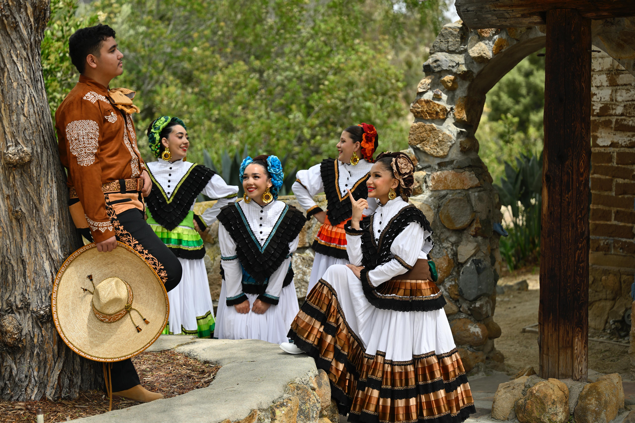 Young dancers in traditional Mexican attire engage with a male figure, showcasing cultural heritage through vibrant costumes and joyful expressions.